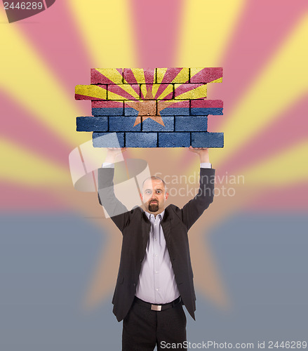 Image of Businessman holding a large piece of a brick wall