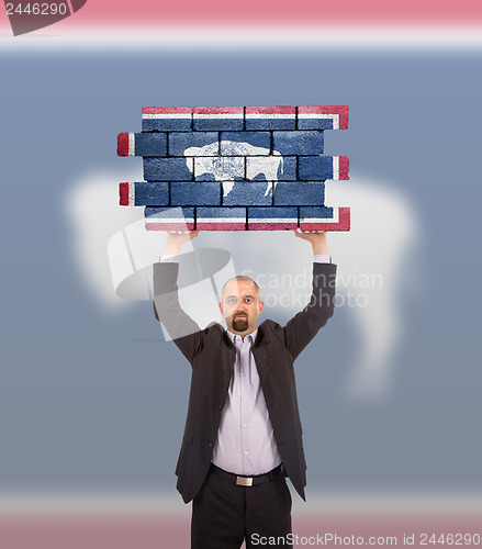 Image of Businessman holding a large piece of a brick wall