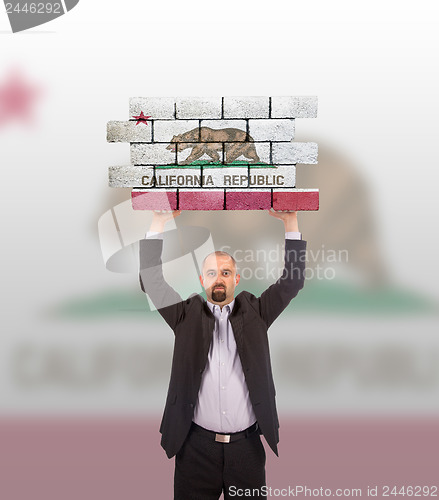 Image of Businessman holding a large piece of a brick wall