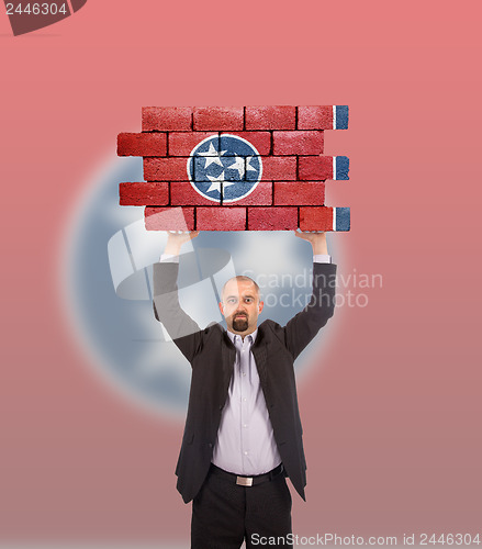 Image of Businessman holding a large piece of a brick wall