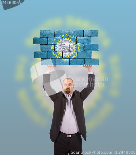 Image of Businessman holding a large piece of a brick wall