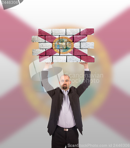 Image of Businessman holding a large piece of a brick wall