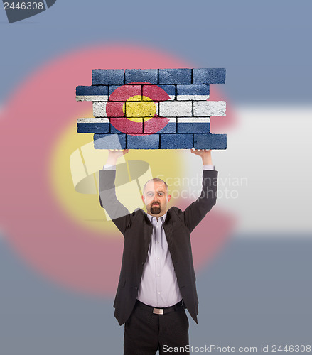 Image of Businessman holding a large piece of a brick wall