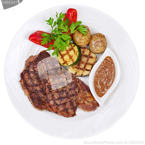 Image of Grilled steaks, baked potatoes and vegetables on white plate on 