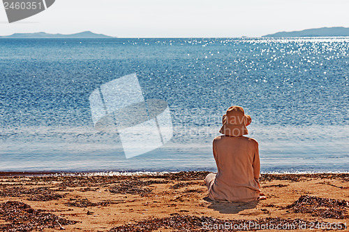 Image of Portrait of young woman on the beach near the sea sitting wearin