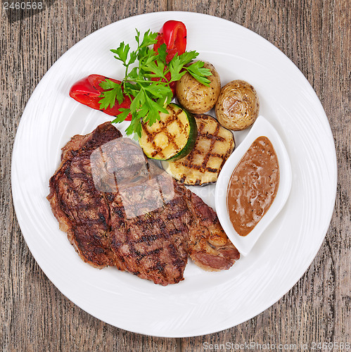 Image of Grilled steaks, baked potatoes and vegetables on white plate on 