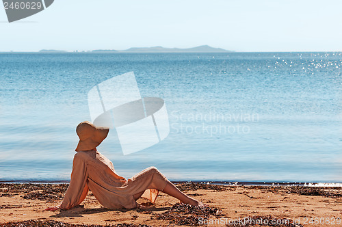 Image of Portrait of young woman on the beach near the sea sitting wearin