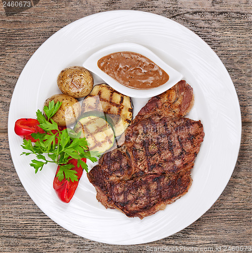 Image of Grilled steaks, baked potatoes and vegetables on white plate on 