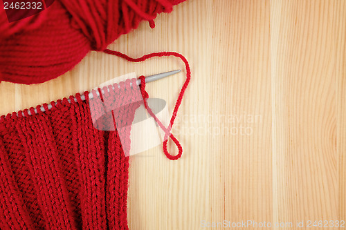 Image of Red knitting in rib stitch with a ball of yarn