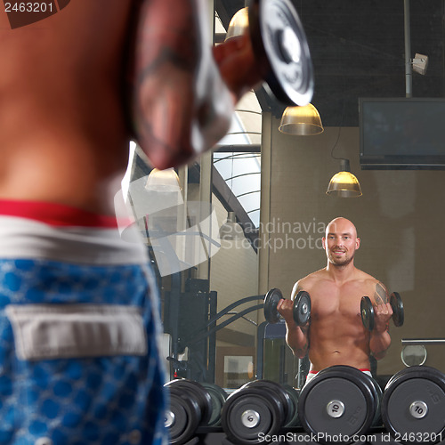 Image of Mirror reflection of two men exercising in gym