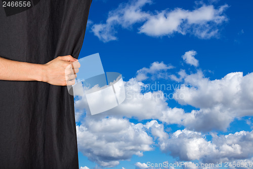 Image of Hand opening black curtain with sky behind it