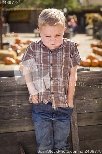 Image of Frustrated Boy at Pumpkin Patch Farm Standing Against Wood Wagon