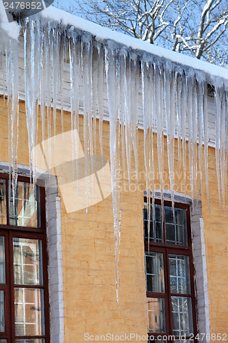 Image of Snow-covered roof with big icicles in winter day