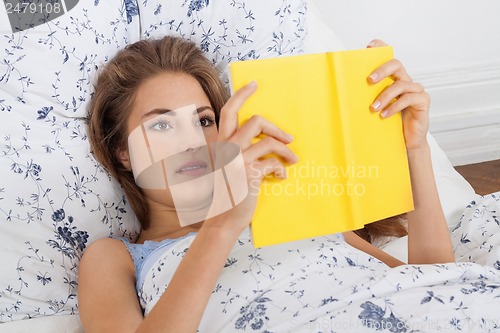 Image of young attractive woman reading book lying in bed