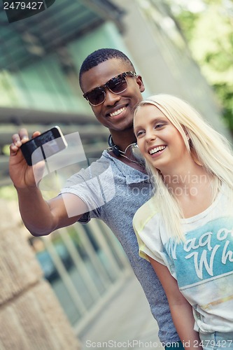 Image of young smiling multiracial couple taking foto by smartphone 