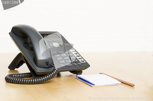 Image of phone on desk with notepad on wooden desk