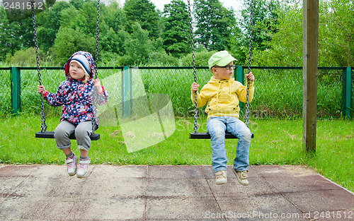 Image of Young children, a boy with a girl swinging on a swing