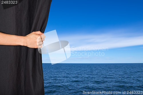 Image of Hand opening black curtain with sea and sky behind it