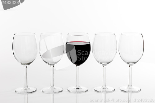 Image of Glass of red wine in a row of empty glasses
