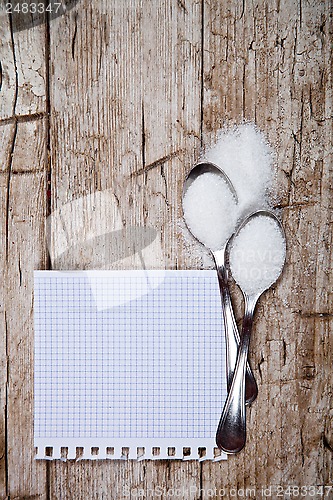 Image of sugar in two spoons and piece of paper 