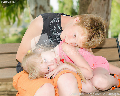 Image of Brother and sister curled up together on the bench in park