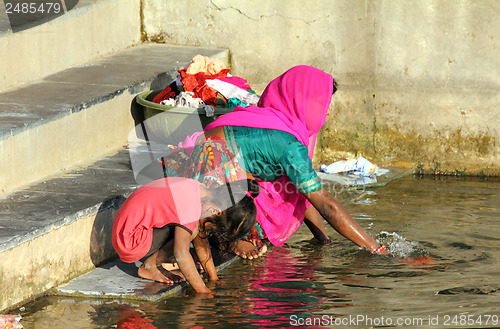 Image of Indian woman with daughter washing clothes in lake