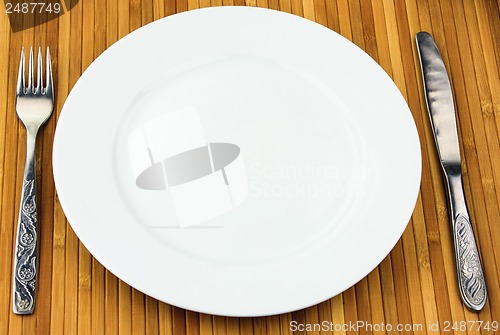 Image of white plate, knife and fork at bamboo napkin