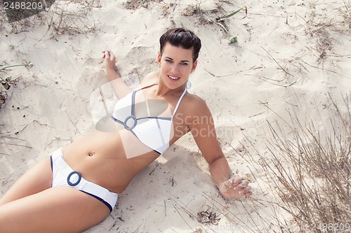 Image of happy young woman sitting in sand dunes beach 