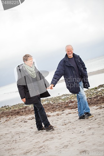 Image of mature happy couple walking on beach in autumn