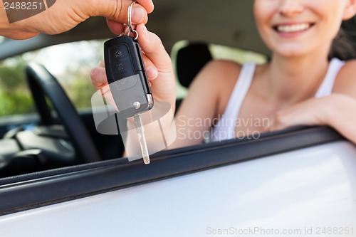 Image of young smiling woman sitting in car taking key 