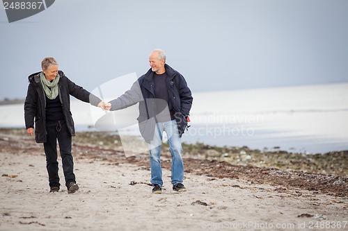 Image of mature happy couple walking on beach in autumn