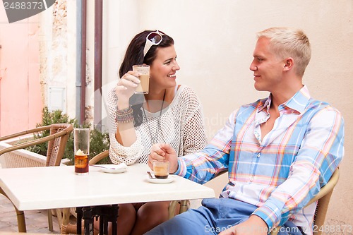 Image of happy young couple sitting outside cafe restaurant drinking coffee 