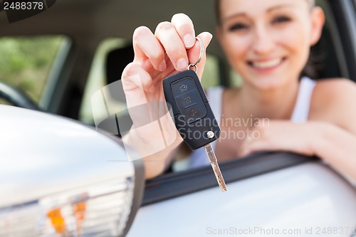 Image of young smiling woman sitting in car taking key 