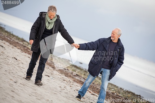 Image of mature happy couple walking on beach in autumn
