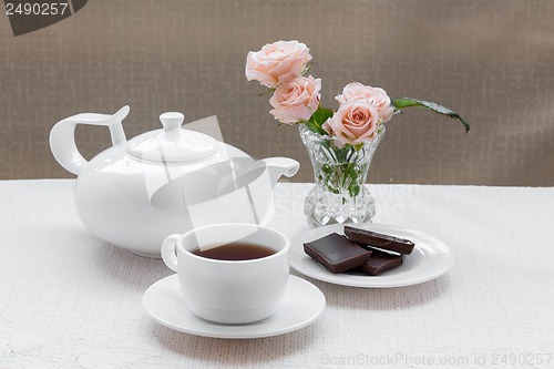 Image of teapot, cup, roses, and chocolate on a plate