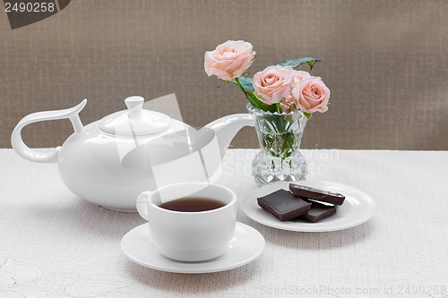 Image of teapot, cup, roses, and chocolate on a plate