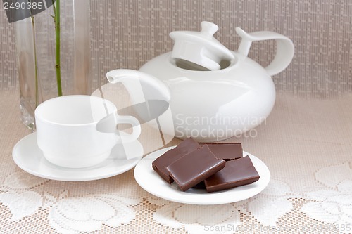 Image of teapot, cup and chocolate on a plate