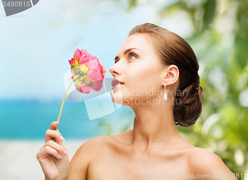 Image of woman wearing earrings and smelling flower