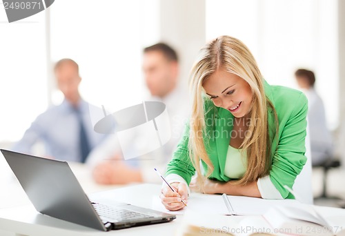 Image of attractive businesswoman taking notes in office