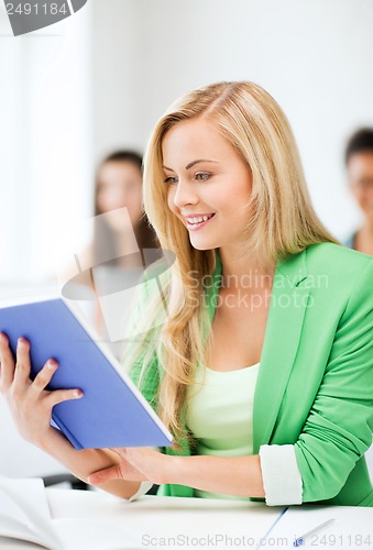 Image of smiling young girl reading book at school