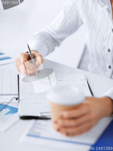 Image of woman filling in blank paper and drinking coffee