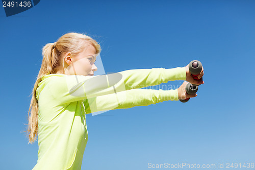 Image of sporty woman with light dumbbells outdoors