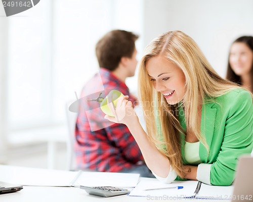 Image of smiling student girl eating apple at school