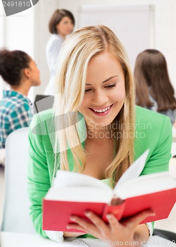 Image of smiling student girl reading book at school