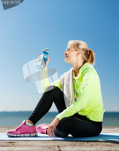 Image of woman drinking water after doing sports outdoors