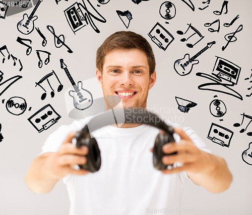 Image of young smiling man offering headphones