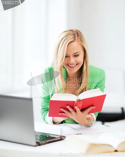 Image of smiling student girl reading book in college