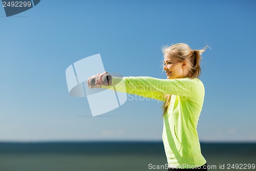 Image of sporty woman with light dumbbells outdoors