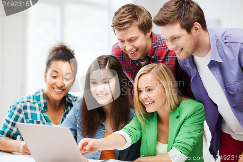 Image of smiling students looking at laptop at school