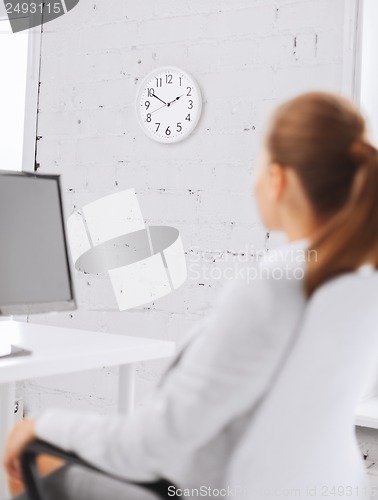 Image of businesswoman looking at wall clock in office